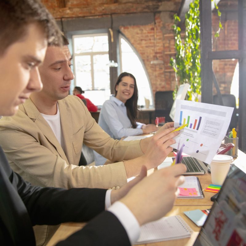 Colleagues working together in a office using modern devices during creative meeting. Stationery, laptop, documents. Concept of business, office, finance, open space.